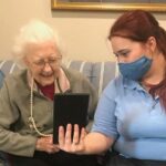 Assisted Living staff helping the old woman watching the tablet