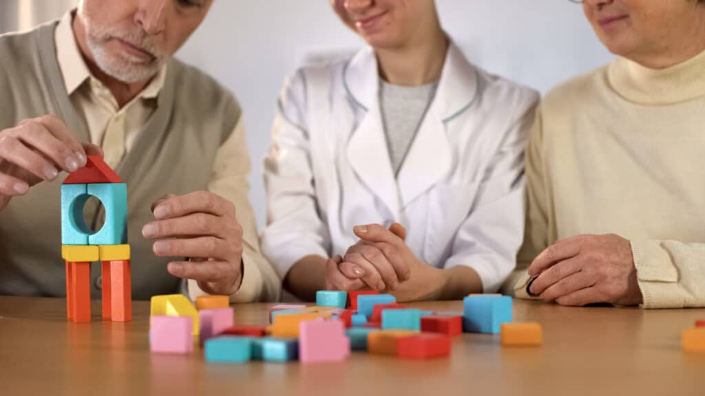 Nurse supporting sick male making house of color wooden cubes, rehabilitation